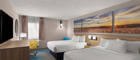 A hotel room with two beds, a desk, a TV, and a large window with a view of a sunset.
