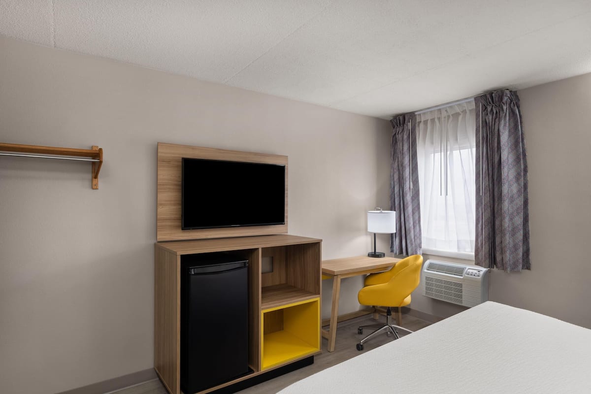 A hotel room with a bed, a desk, a television, a refrigerator, a chair, and a window with curtains.