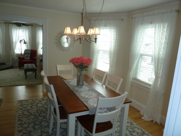 A dining room with a wooden table, white chairs, a vase with flowers, and a chandelier. - Portsmouth. Beautiful 2 BR Condo. Great Location. Short Walk To Market Square. (Portsmouth)