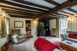 A cozy living room with a high ceiling, exposed beams, a fireplace, and a seating area with a sofa and armchairs. - Yew Tree Cottage- Sleeps 12, Garden & Pet-friendly (Newport Pagnell)