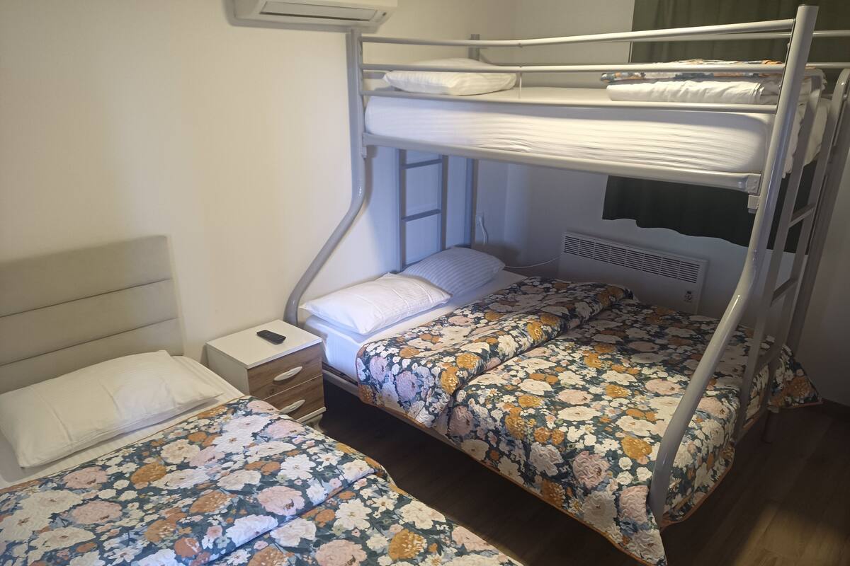 Une chambre avec un lit superposé doté d’une tête de lit en bois, d’une table de chevet avec une télécommande et d’une literie à motifs floraux.