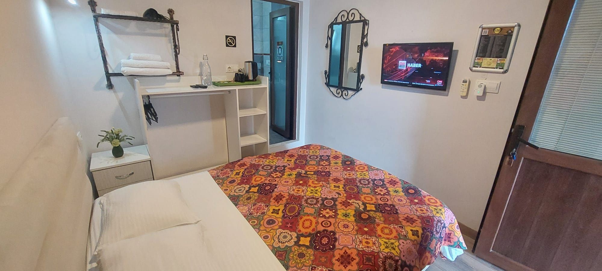 A bedroom with a bed, a desk, a mirror, a television, and a door.