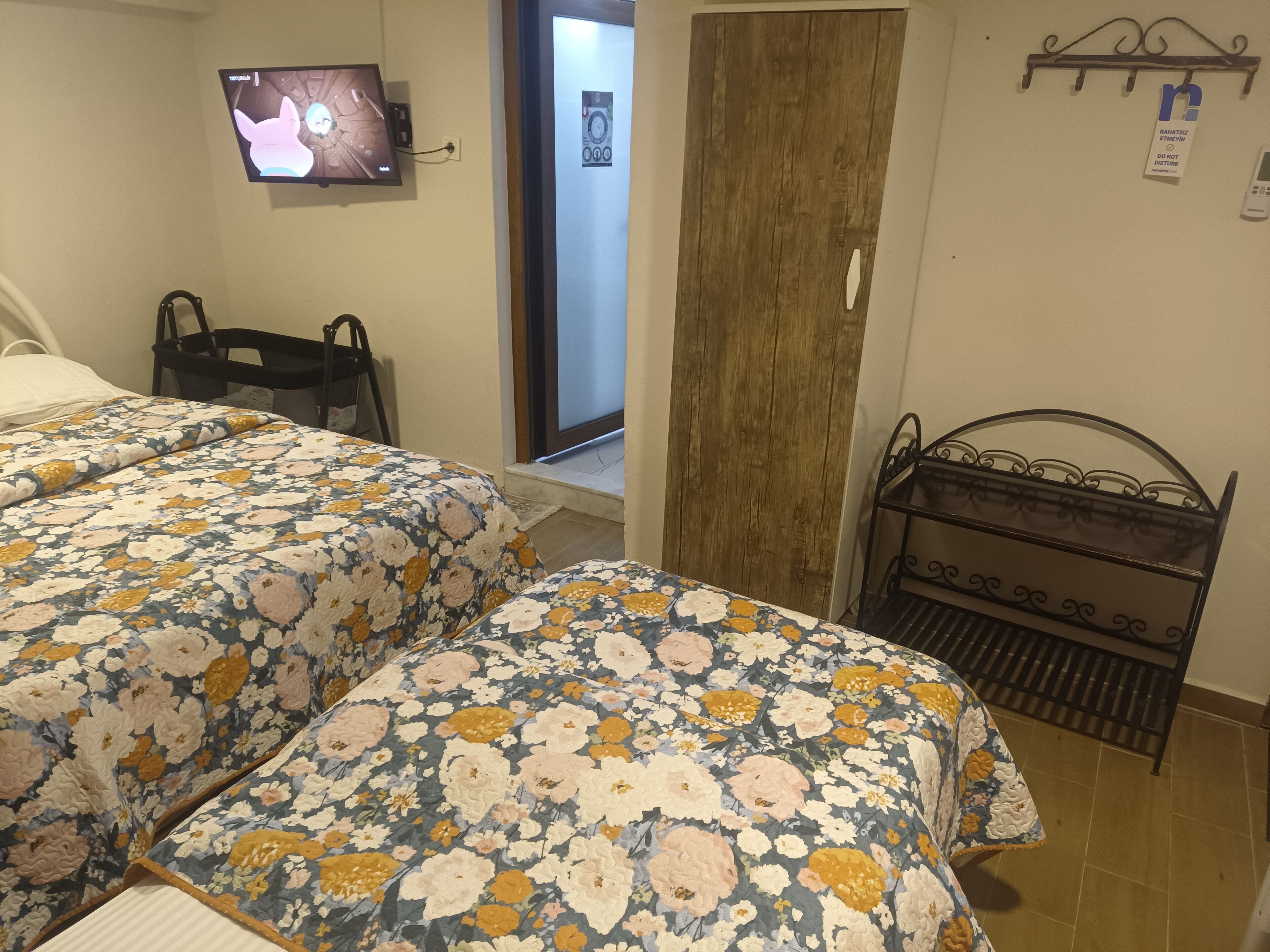 Un dormitorio con dos camas, un televisor montado en la pared, una puerta de madera y un perchero metálico con ganchos.