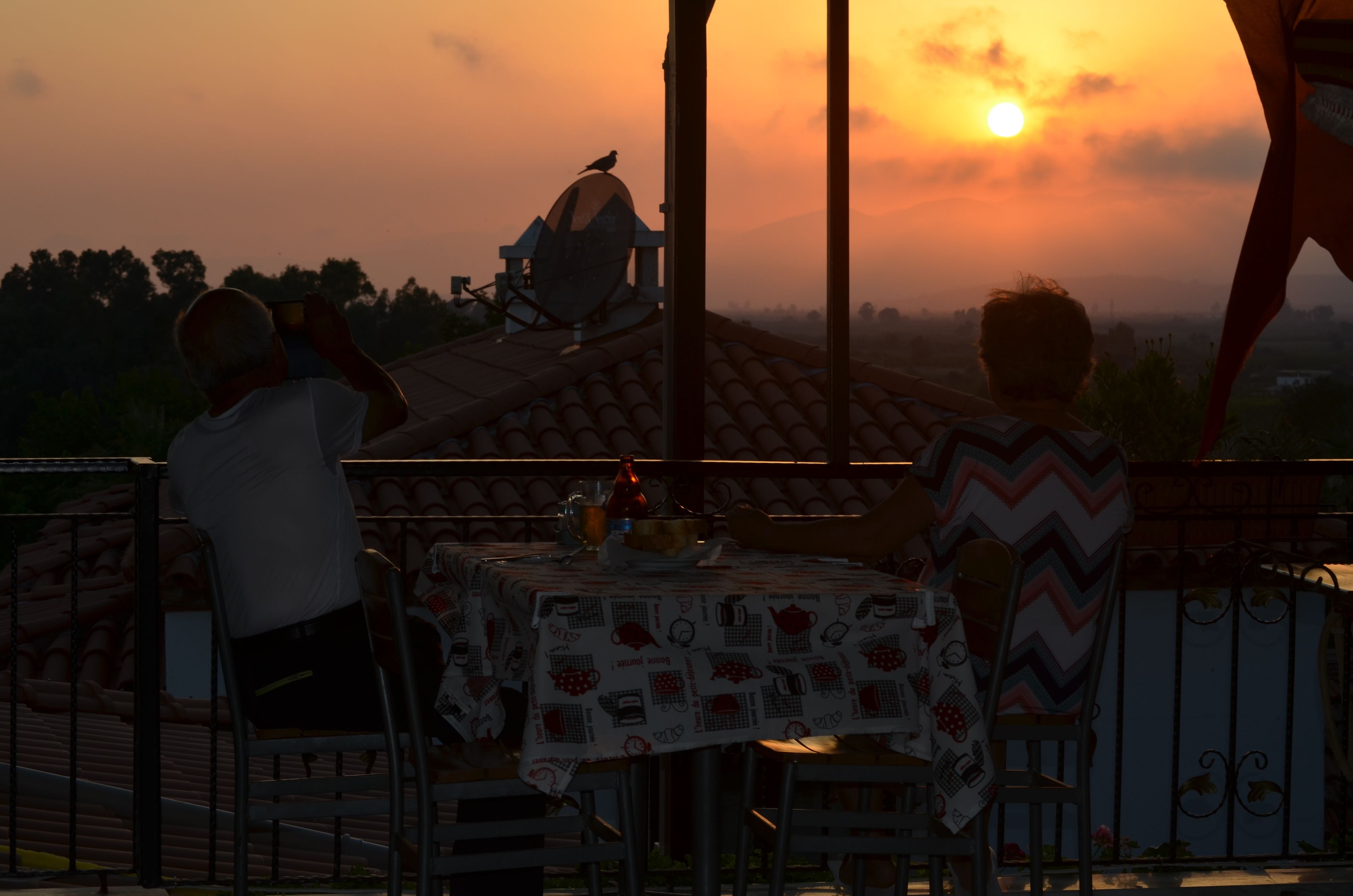A terrace with a table set for two, overlooking a sunset.