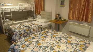 Un dormitorio con literas, dos camas individuales con ropa de cama estampada, una mesita con una tetera y un aire acondicionado de pared.