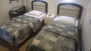 A hotel room with two beds, each with a quilted bedspread and a headboard. There is a nightstand with a lamp and a small table with a plant.