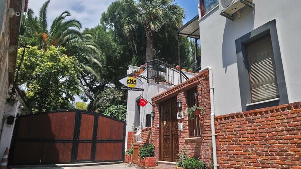 A building with a brick facade, a wooden gate, and a balcony with potted plants.