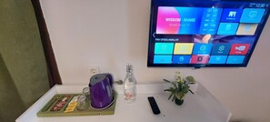 A room with a flat-screen TV displaying a smart TV interface, a remote control, a glass bottle, a purple kettle, and a small potted plant on a white table. - Ena Serenity Boutique Hotel (Selçuk)