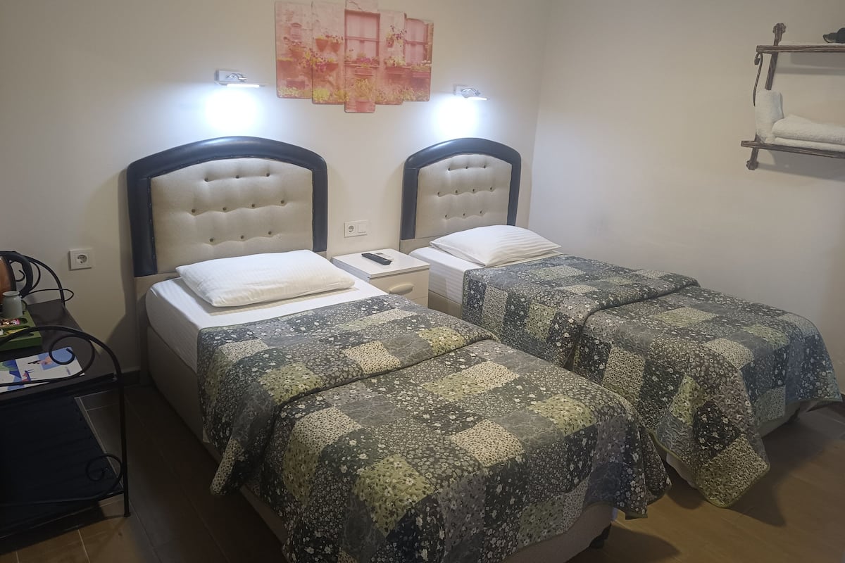 Une chambre avec deux lits, chacun doté d’une tête de lit et d’une table de chevet. Une étagère est fixée au mur au-dessus des lits.
