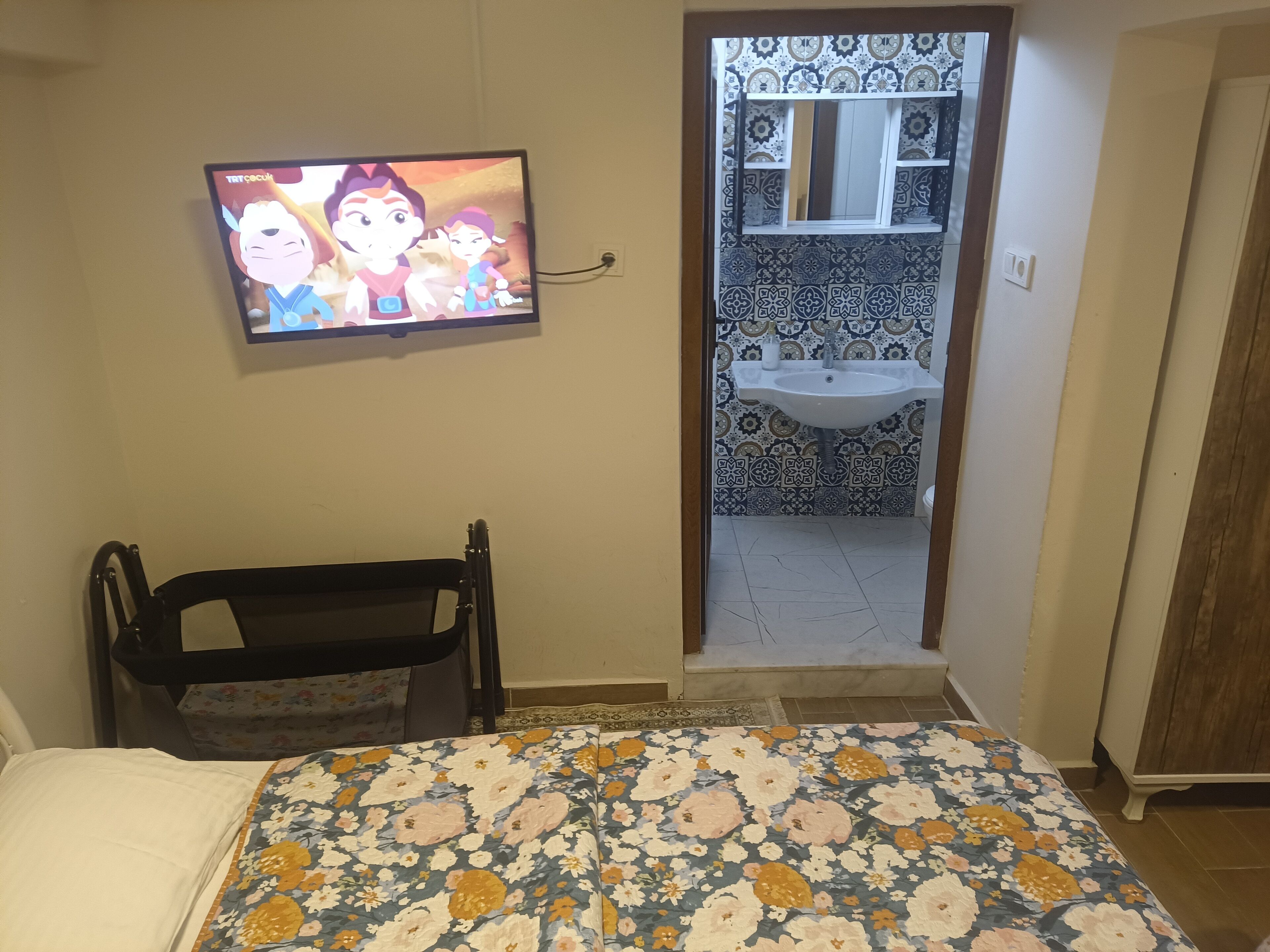 A bedroom with a bed, a television, a bathroom with a sink, and a patterned floor.