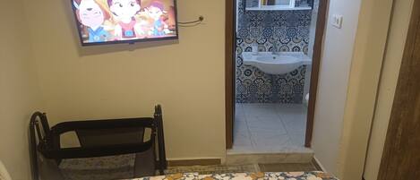 A bedroom with a bed, a television, a bathroom with a sink, and a patterned floor.