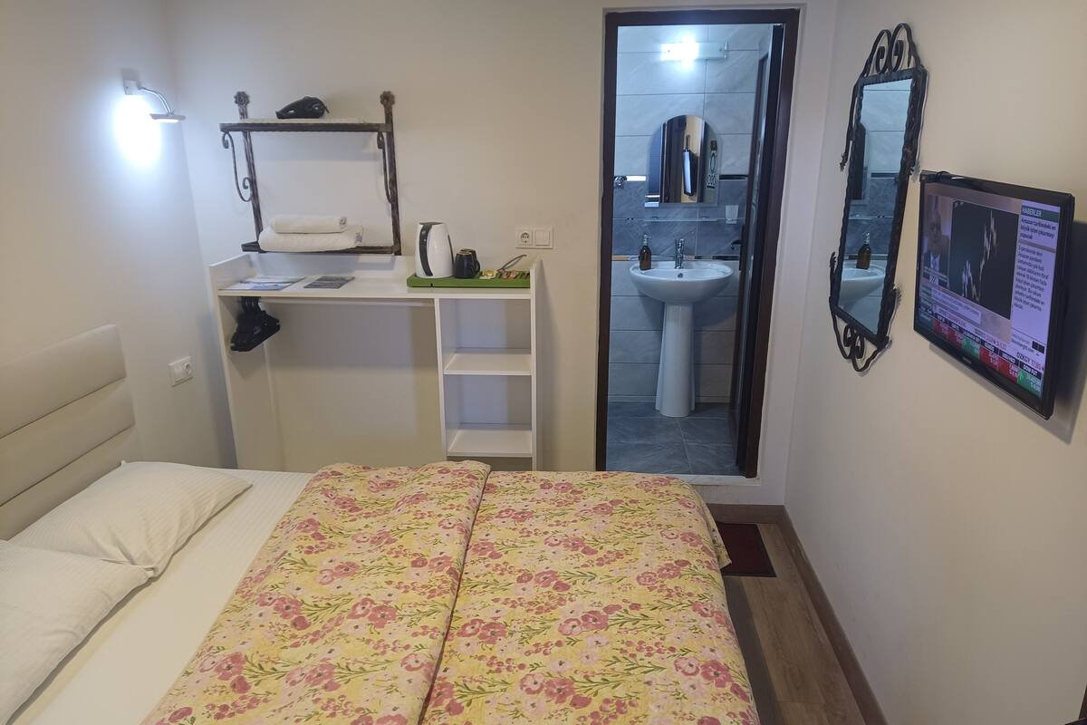 Une chambre à coucher avec un lit, une table de chevet, une étagère avec une serviette, un miroir et un téléviseur.