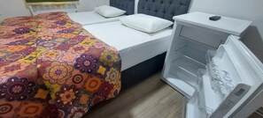 A bedroom with a bed, a bedside table, a white pillow, a patterned bedspread, and a white appliance. - Ena Serenity Boutique Hotel (Selçuk)