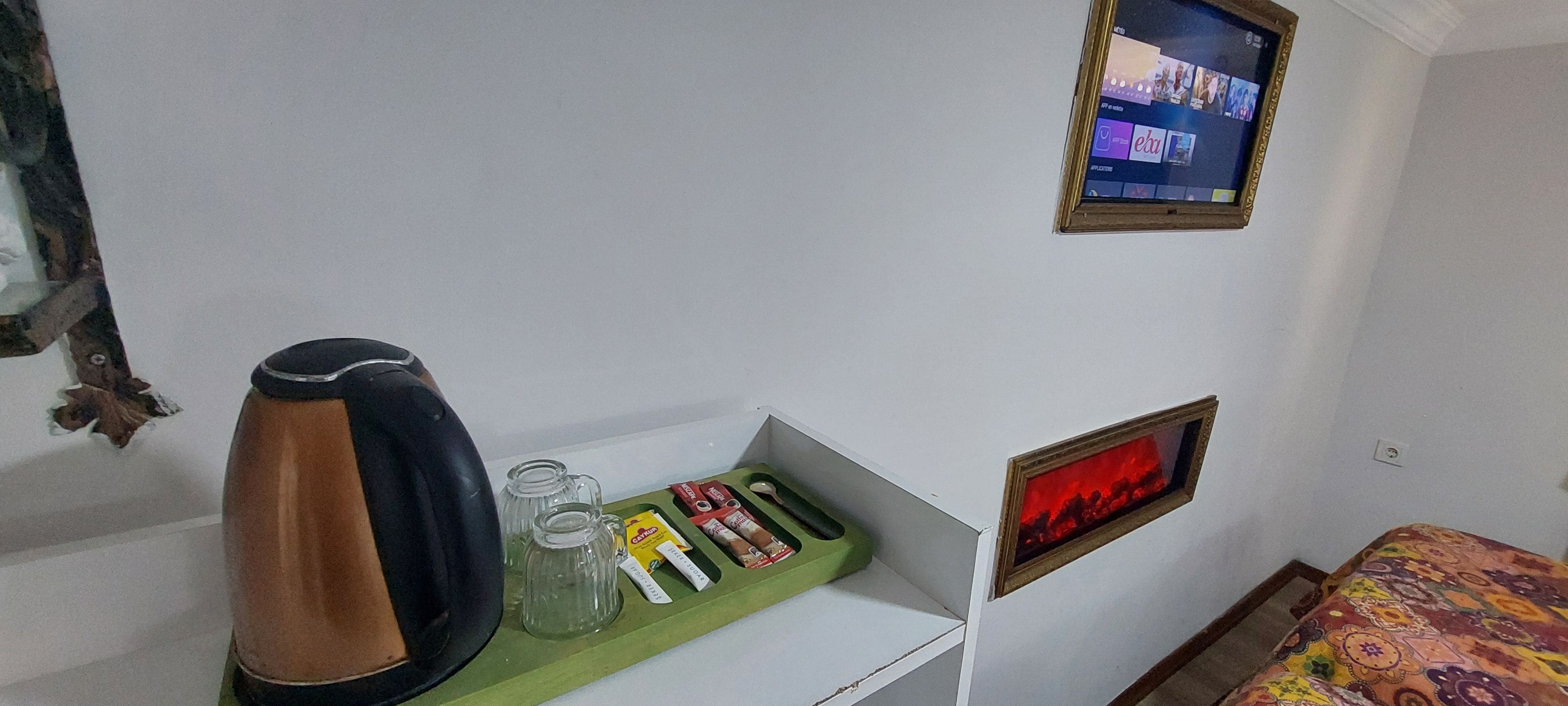 Une chambre comprenant un lit, une petite table avec une bouilloire, un plateau avec des collations, une télévision et un radiateur fixé au mur.