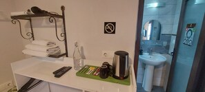Une chambre d’hôtel avec un comptoir blanc, un porte-serviettes, une bouteille, une bouilloire, une télécommande et un plateau vert contenant des articles de toilette.