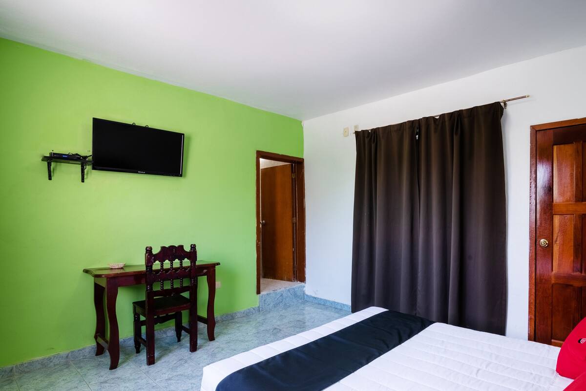 A bedroom with a bed, a desk, a chair, a television, and a door.