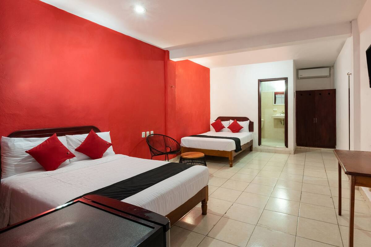A hotel room with two beds, red walls, a wooden floor, and a small table.