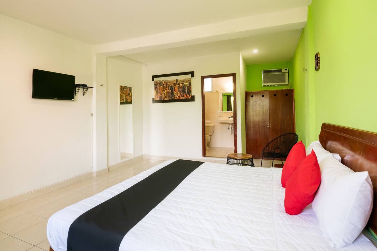 A hotel room with a bed, a TV mounted on the wall, a door leading to a bathroom, and a green wall.