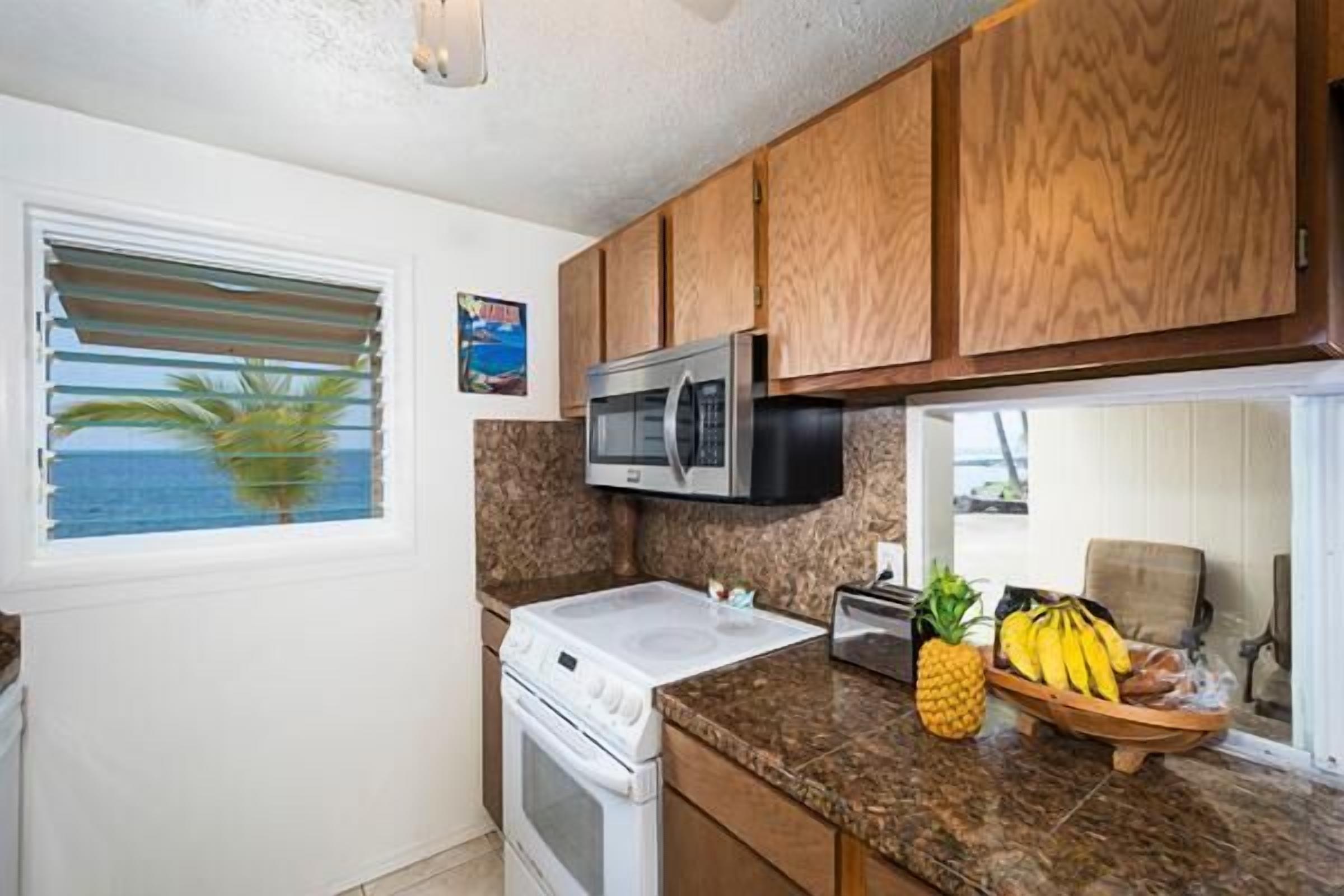 A kitchen with wooden cabinets, a microwave, a stove, and a window with blinds.