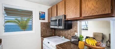 A kitchen with wooden cabinets, a microwave, a stove, and a window with blinds.