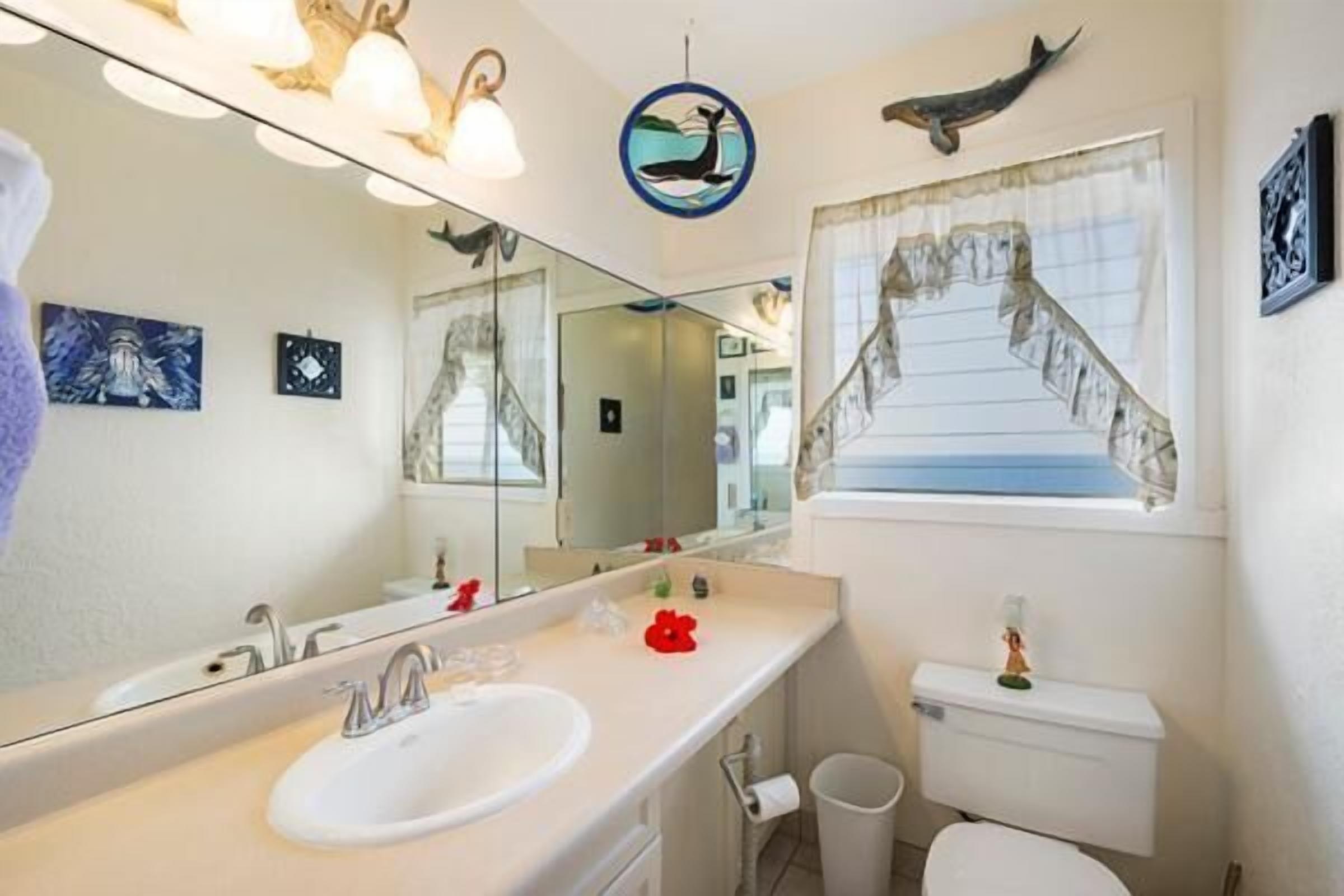 Une salle de bain avec un grand miroir, un lavabo, des toilettes et une fenêtre donnant sur la mer.