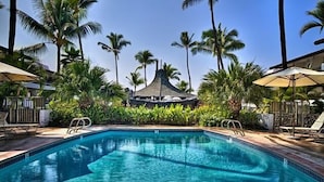 A swimming pool with lounge chairs and umbrellas, surrounded by palm trees and a gazebo.