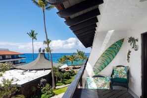 A balcony with a view of the ocean, palm trees, and a surfboard decoration. - Casa De Emdeko 330 (Kailua-Kona)