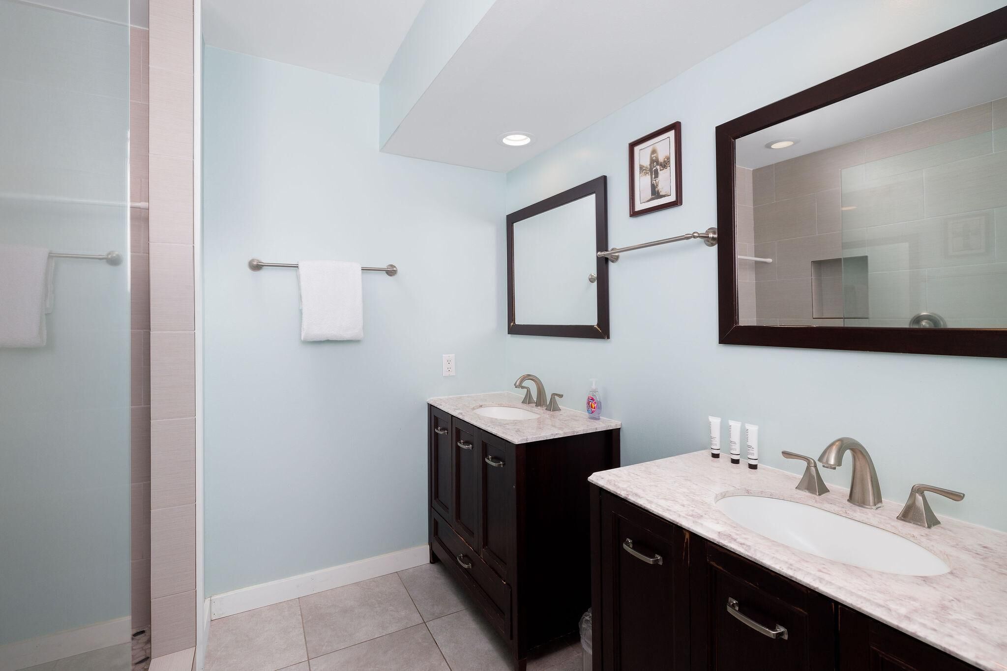 A bathroom with two sinks, dark wooden cabinets, a large mirror, and a glass shower enclosure.