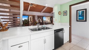 A modern kitchen with white cabinetry, a stainless steel sink, and a black dishwasher. - Kona Coast Resort at Keauhou Gardens 8204 (Kailua-Kona)