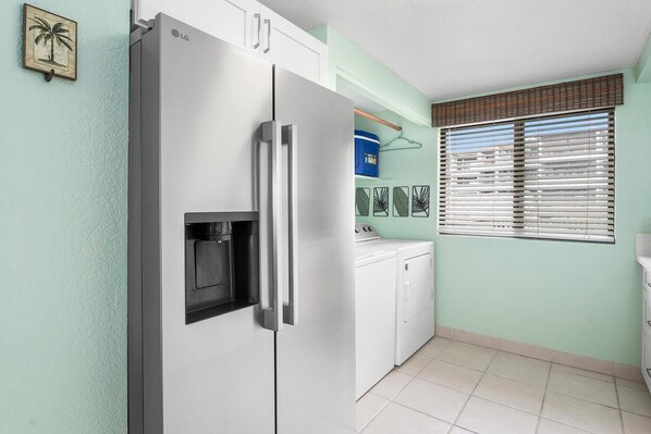Uma cozinha compacta com geladeira embutida da LG, máquina de lavar e janela com persianas.