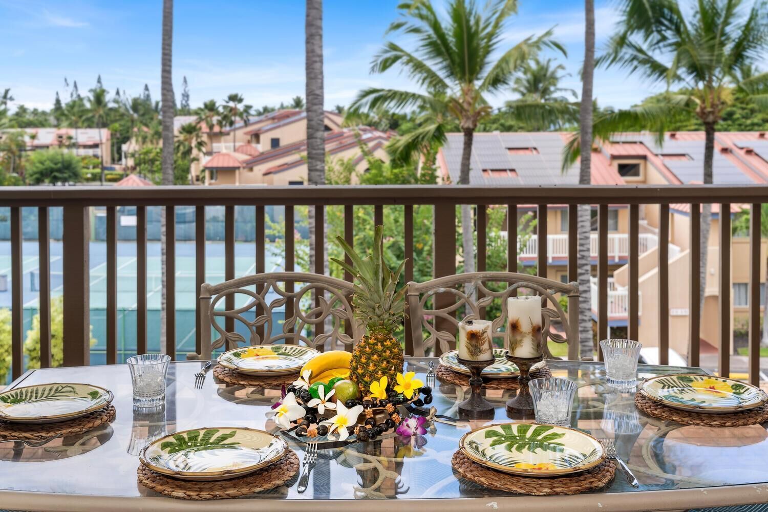 A dining table set with plates, cutlery, and a pineapple centerpiece, overlooking a scenic view with palm trees and buildings.