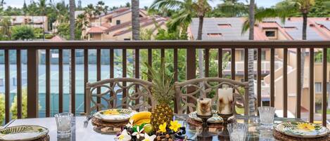 A dining table set with plates, cutlery, and a pineapple centerpiece, overlooking a scenic view with palm trees and buildings.
