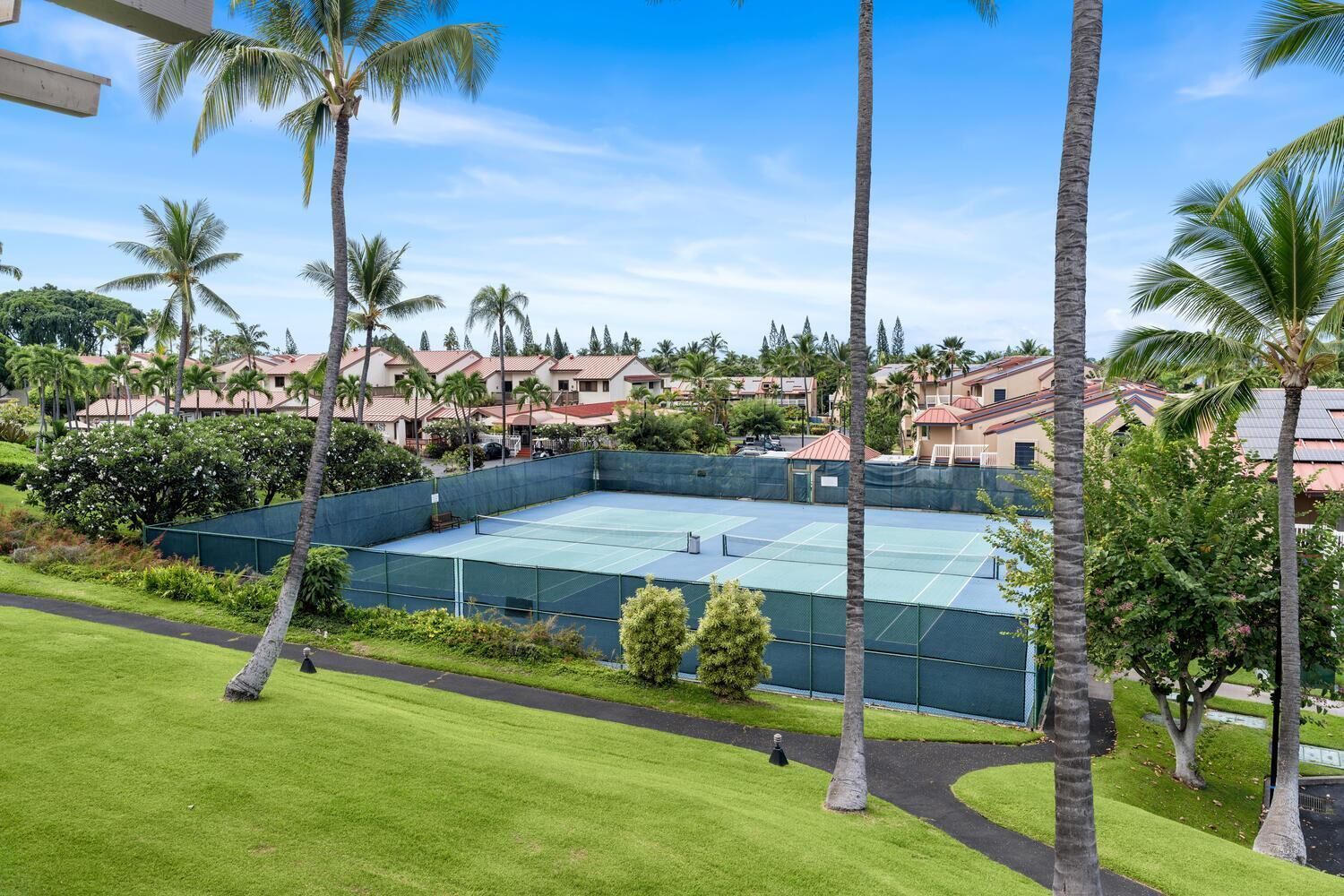 Un court de tennis entouré de palmiers et un quartier résidentiel avec des maisons.