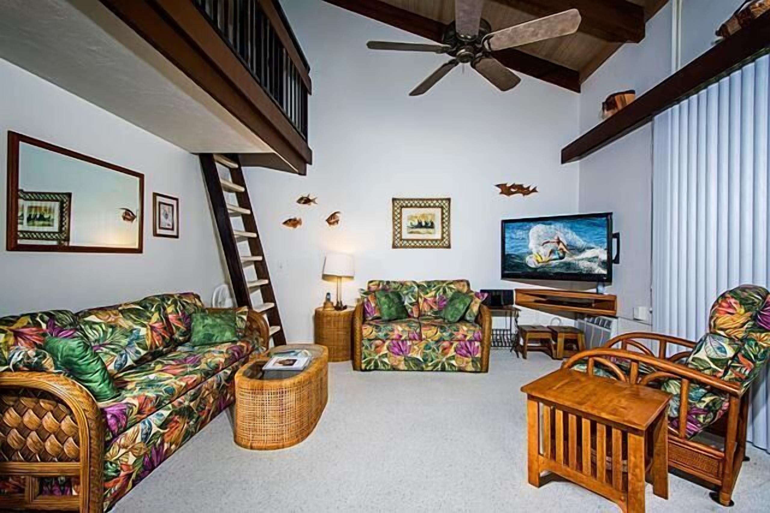 A living room with a sofa, armchairs, a coffee table, a TV, and a ceiling fan.