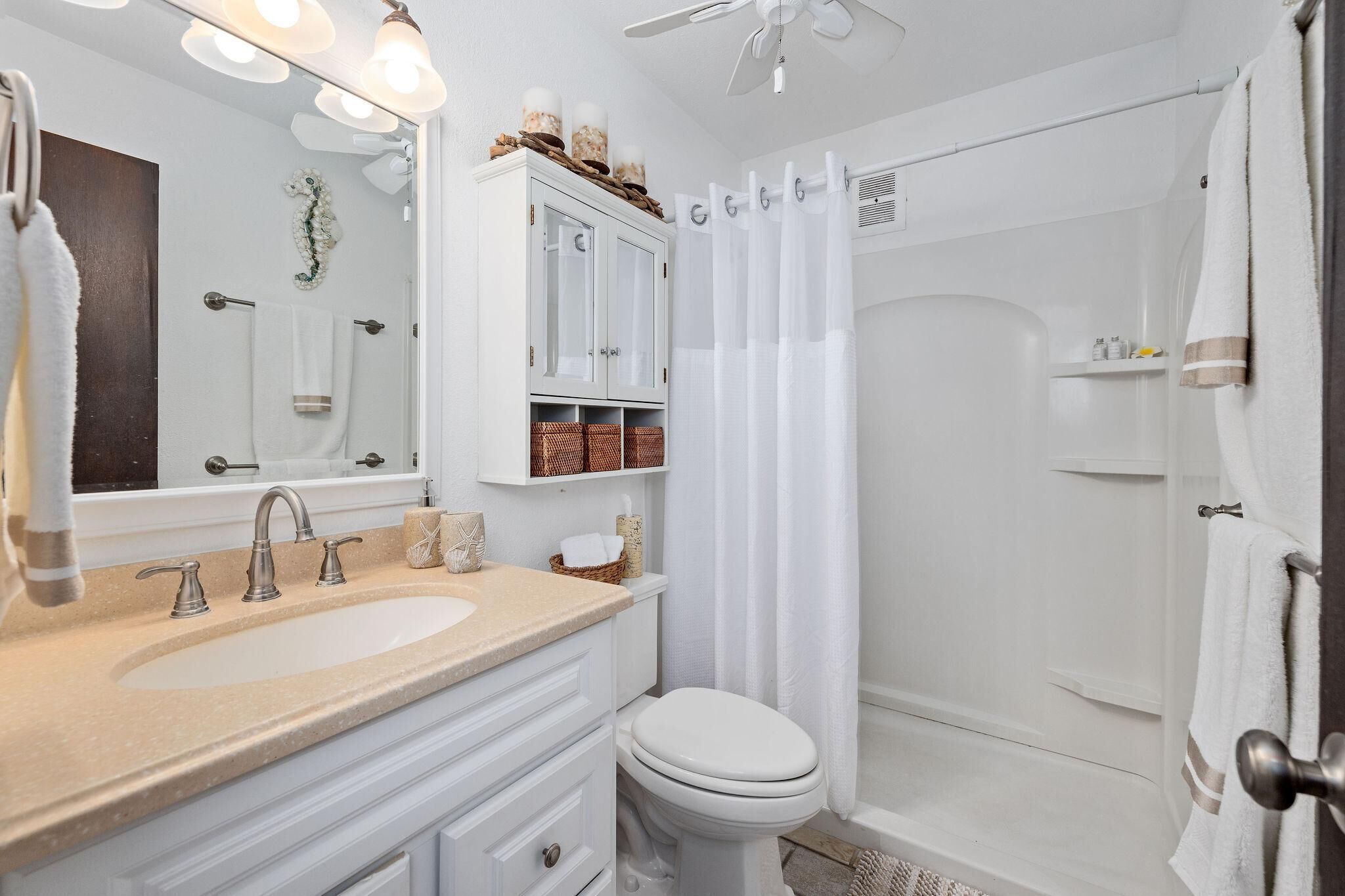 A modern bathroom with a double sink vanity, a toilet, a shower with a glass door, and a ceiling fan.