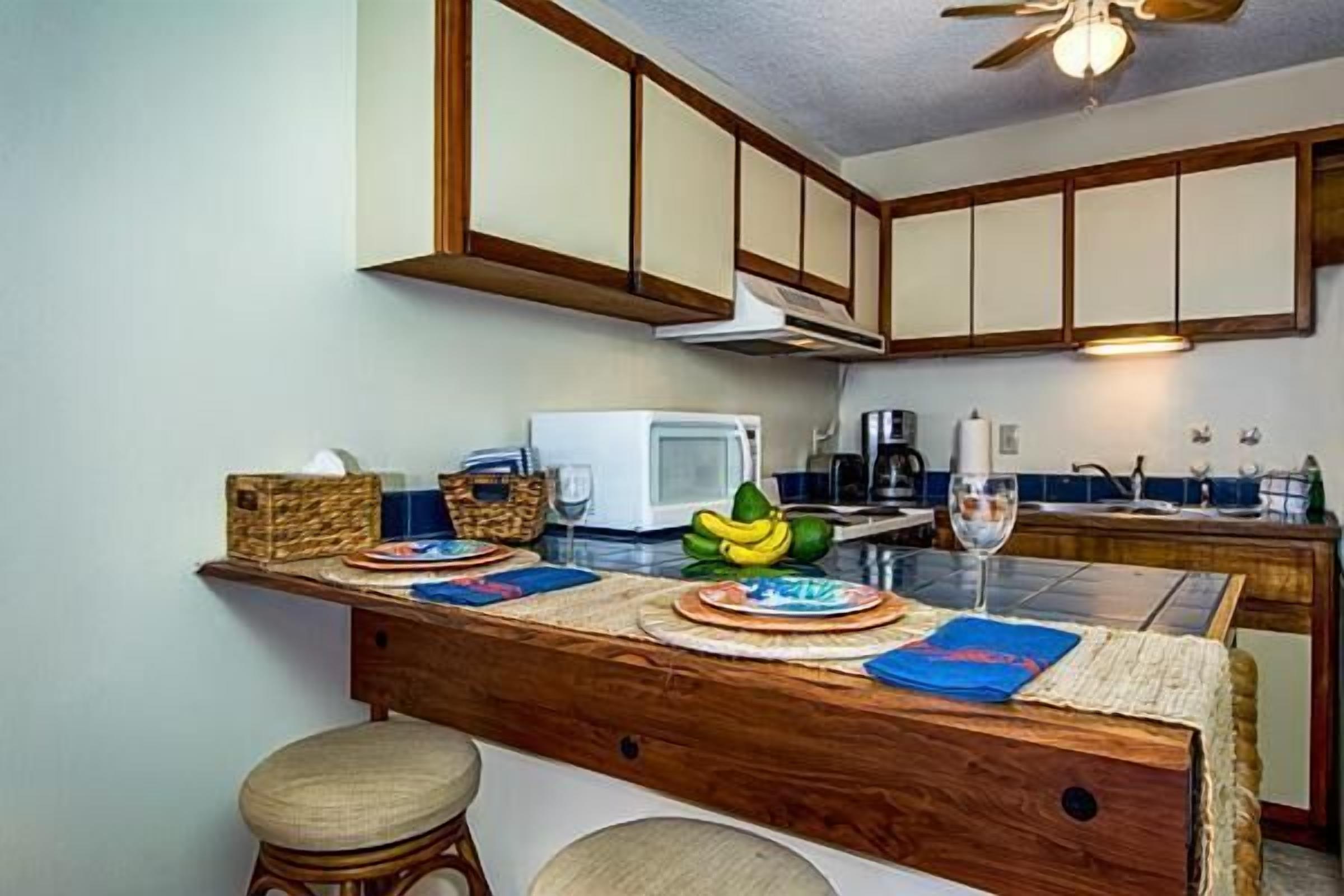 A kitchen with wooden cabinets, a microwave, a coffee maker, and a dining area with stools and a table set for two.