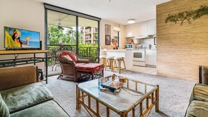 Una sala moderna con una mesa de centro de vidrio, muebles de mimbre, un televisor de pantalla plana y vistas a un balcón con mobiliario exterior.