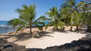 A beach with palm trees, a chair, and a rocky foreground. - Casa De Emdeko 204 (Kailua-Kona)