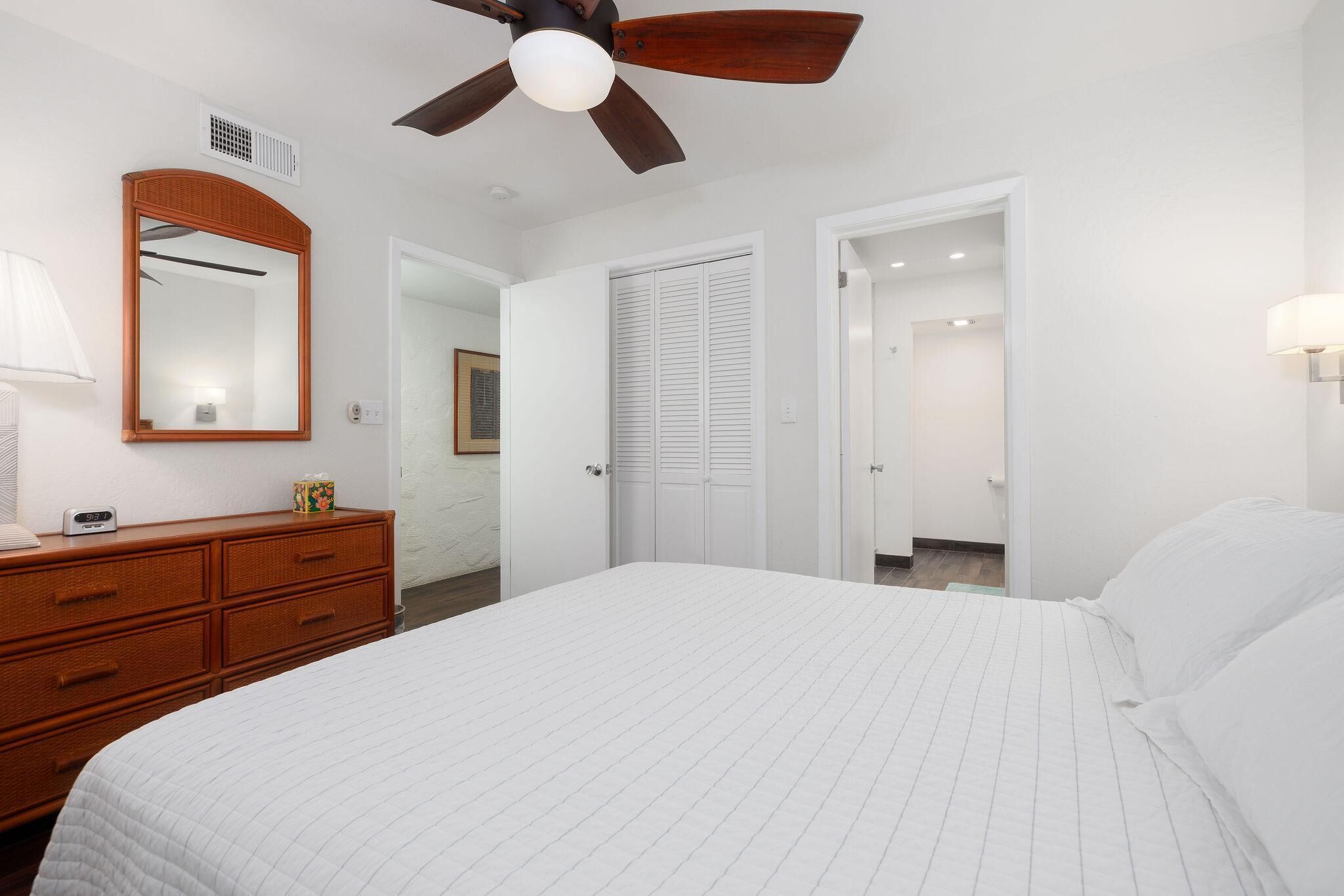 A bedroom with a large bed, a wooden dresser, a ceiling fan, and white doors leading to other rooms.
