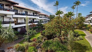 A hotel with multiple balconies, lush gardens, and palm trees. - Casa De Emdeko 204 (Kailua-Kona)