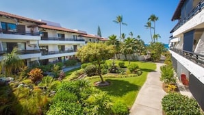 A hotel courtyard with multiple balconies, lush greenery, and a clear sky. - Casa De Emdeko 204 (Kailua-Kona)