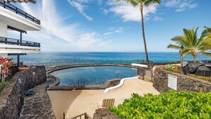 A pool area with a view of the ocean, surrounded by palm trees and a stone wall. - Casa De Emdeko 204 (Kailua-Kona)