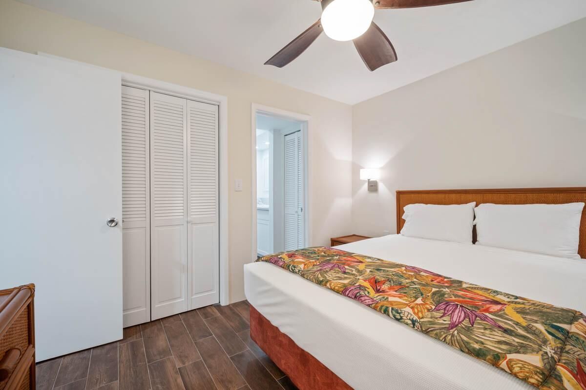 Une chambre à coucher comprenant un lit, un ventilateur de plafond, une table de chevet et une porte dotée de volets à persiennes.