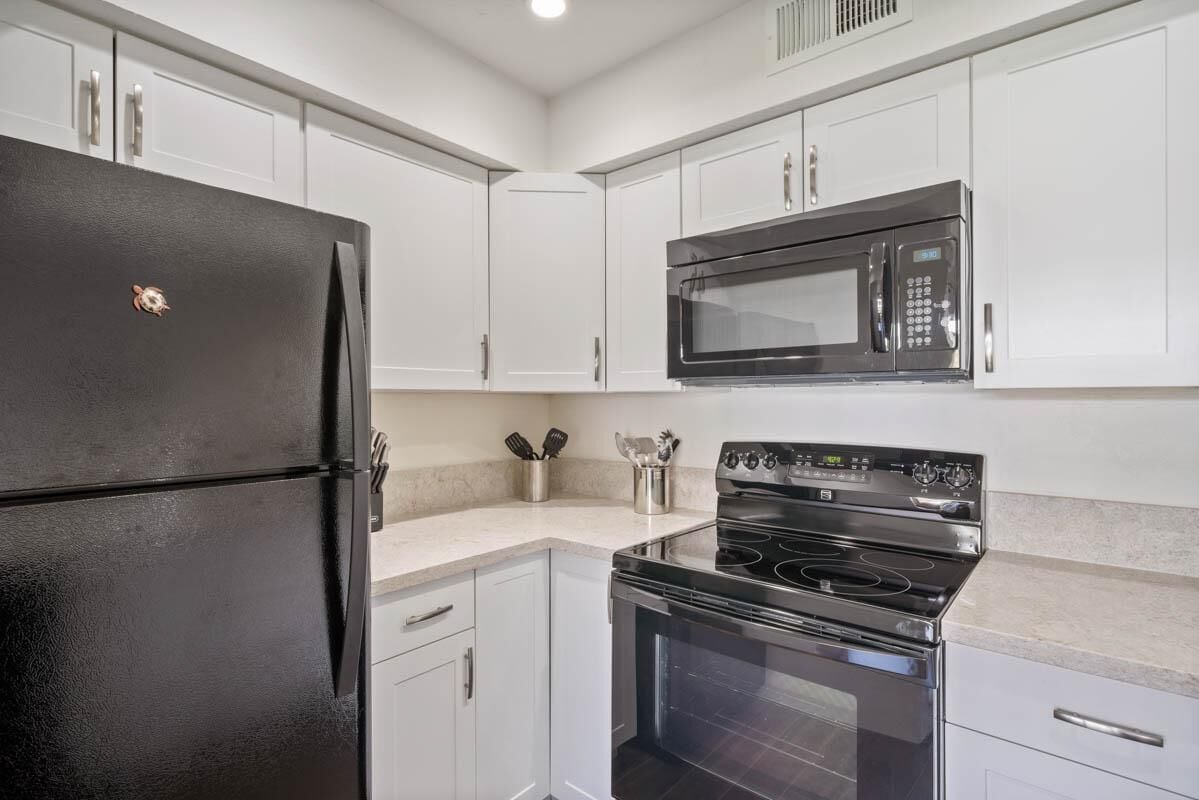 A modern kitchen with white cabinets, a black refrigerator, a microwave, and a stove.