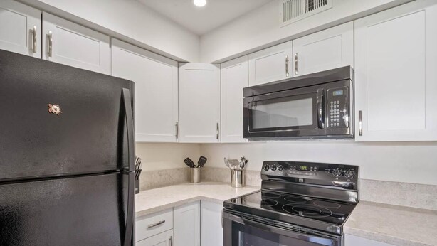A modern kitchen with white cabinets, a black refrigerator, a microwave, and a stove. - Casa De Emdeko 204 (Kailua-Kona)