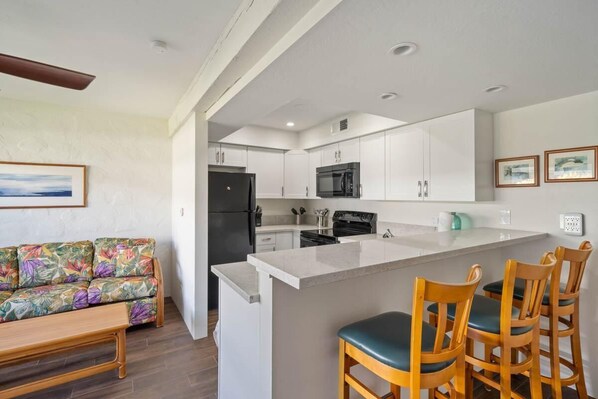 Una cocina moderna con armarios blancos, un refrigerador negro, un microondas y una isla grande con taburetes de bar.