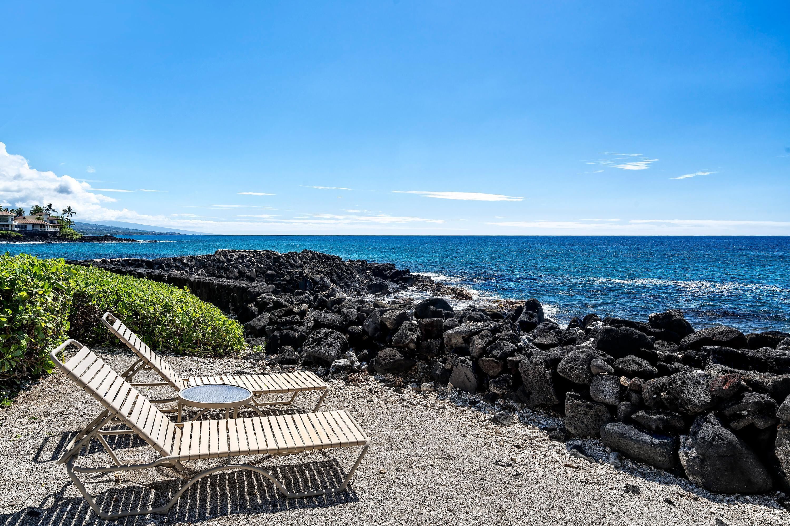 Angolo relax in spiaggia con poltrone e tavolo, circondato da una costa rocciosa e vista sull'oceano.