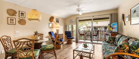 A spacious living area with wicker furniture, a glass coffee table, and a ceiling fan.