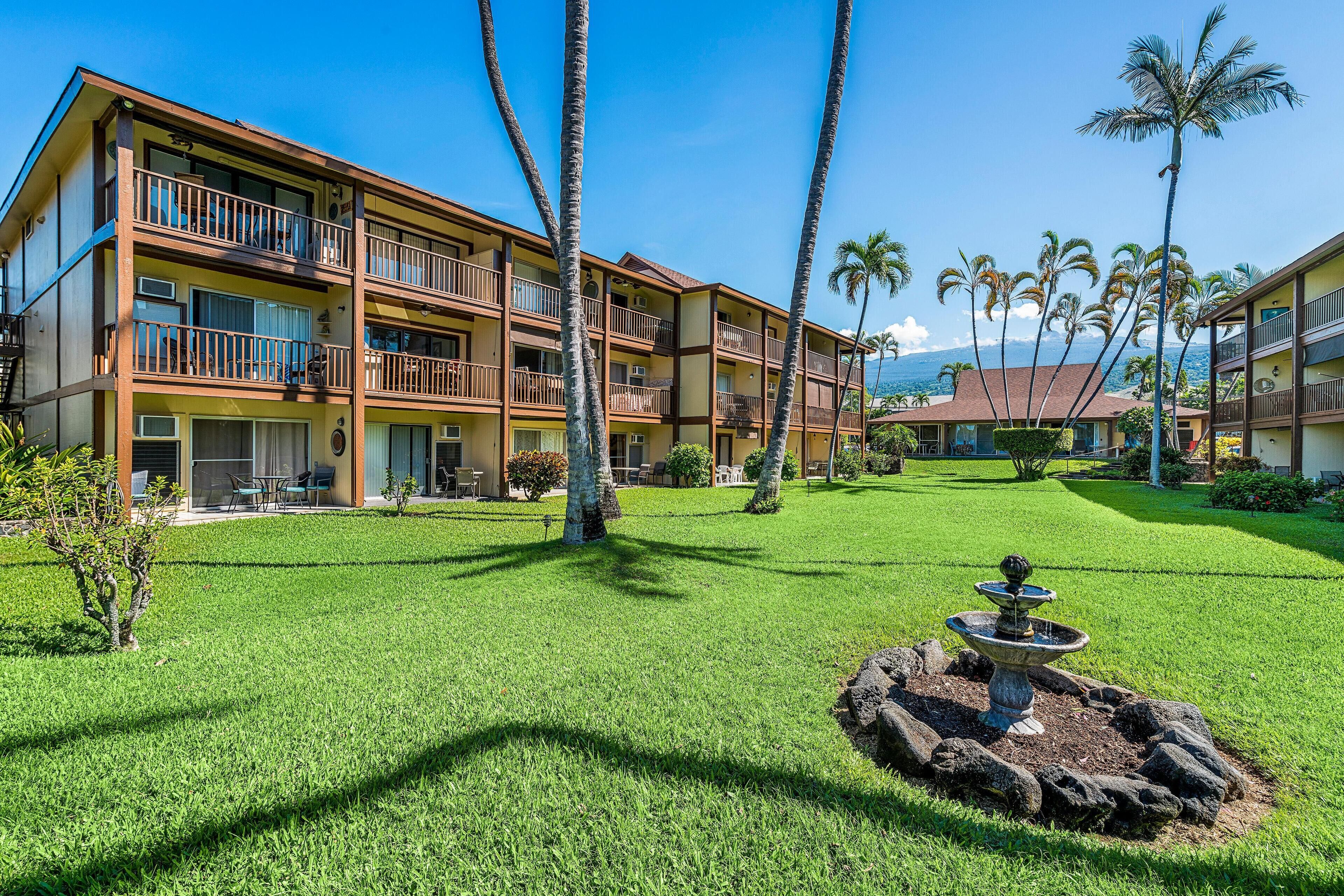 A hotel with multiple balconies, a well-maintained lawn, and a central fountain.