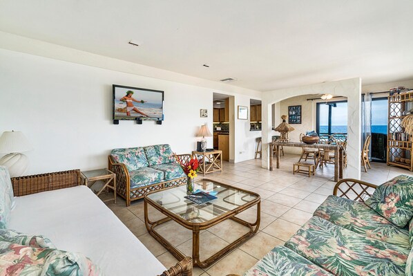 A spacious living room with a sofa, a coffee table, and a dining area with a view of the sea. - Casa De Emdeko 219 (Kailua-Kona)